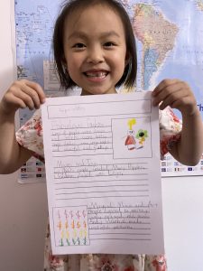 little girl holding up a piece of school work