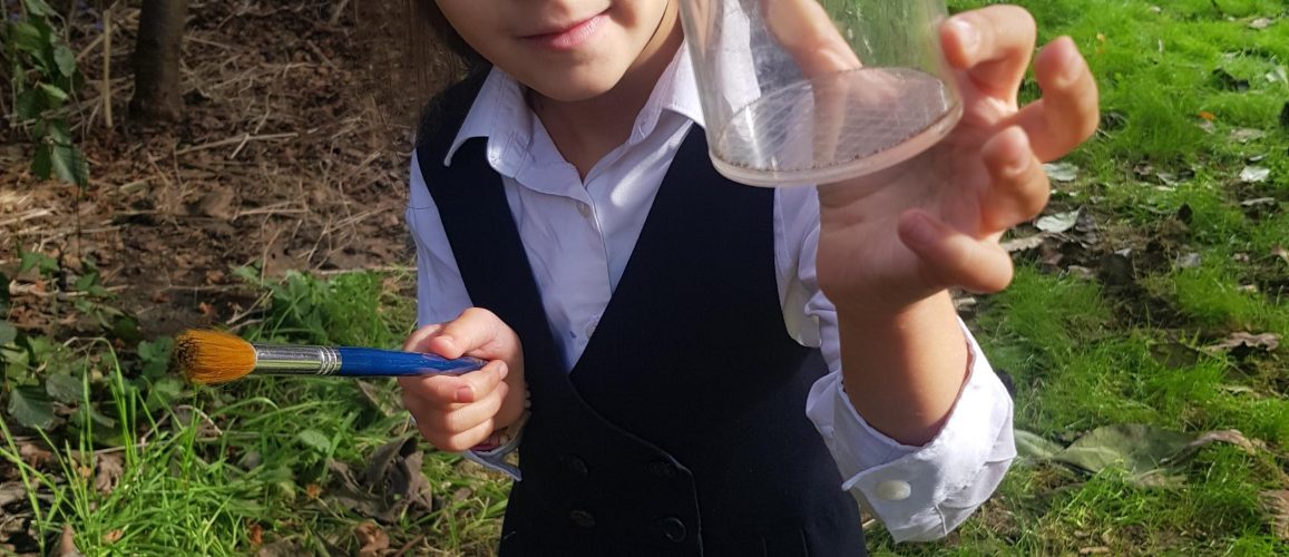 little girl wearing school uniform, holding a plastic pot out to camera