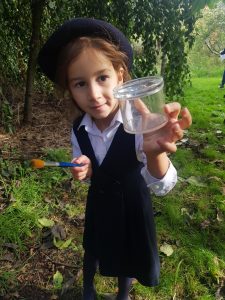 little girl wearing school uniform, holding a plastic pot out to camera