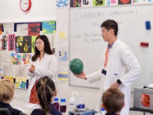 A man and a woman standing at the front of a class in lab coats.