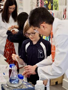 A scientist with a Lyceum pupil showing them how to use a pipette to put liquid into a container