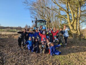 group of children with their thumbs up and a tractor in the background