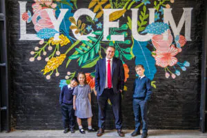 students standing by their teacher, in front of a decorated wall