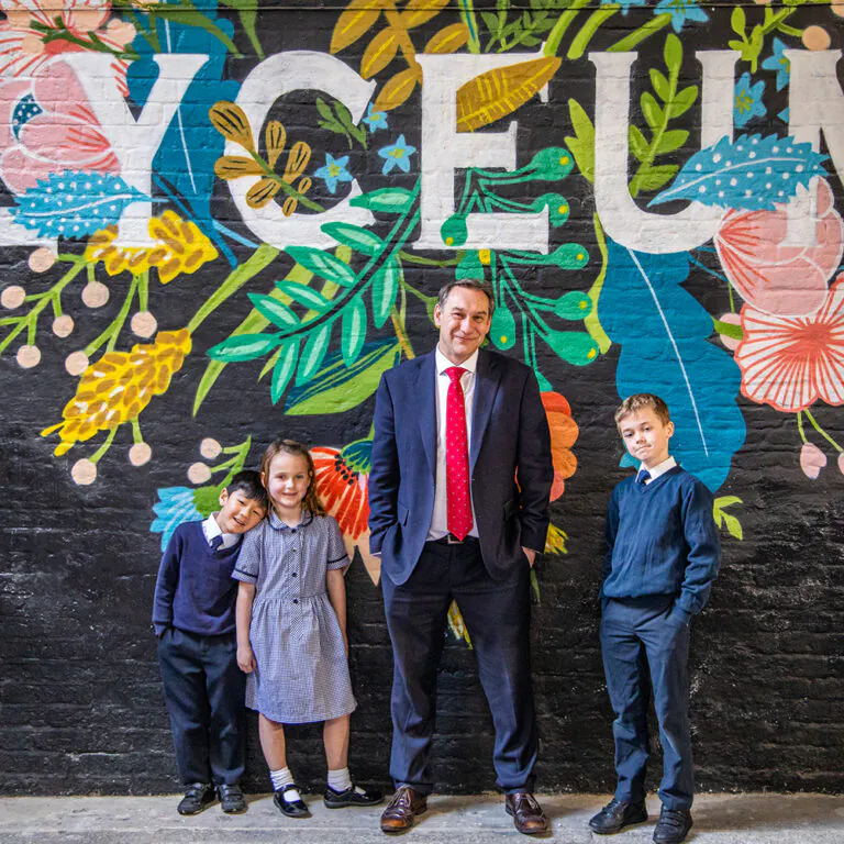 students standing by their teacher, in front of a decorated wall
